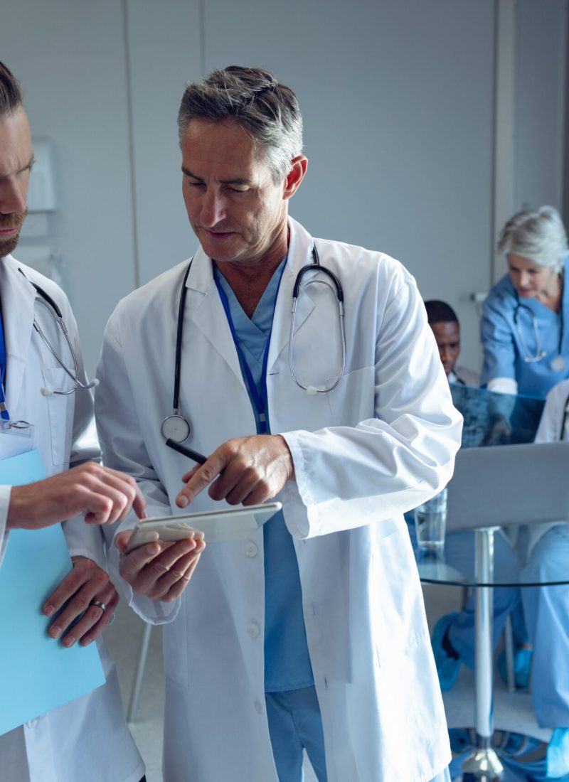 Male doctors discussing over digital tablet at hospital