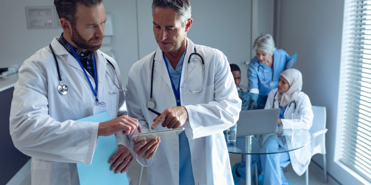 Male doctors discussing over digital tablet at hospital