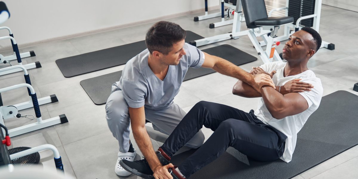 Physiotherapist applying pressure to crossed arms and foot of patient during resisted isometric testing